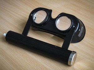 Frenzelbrille, der zylinderförmige Teil enthält die Batterien zur Stromversorgung der Lichtquelle in der Brille.